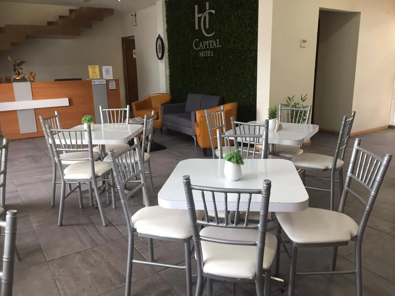Recepción con mostrador de madera, muro verde con el logo, sillones color miel y mesas blancas