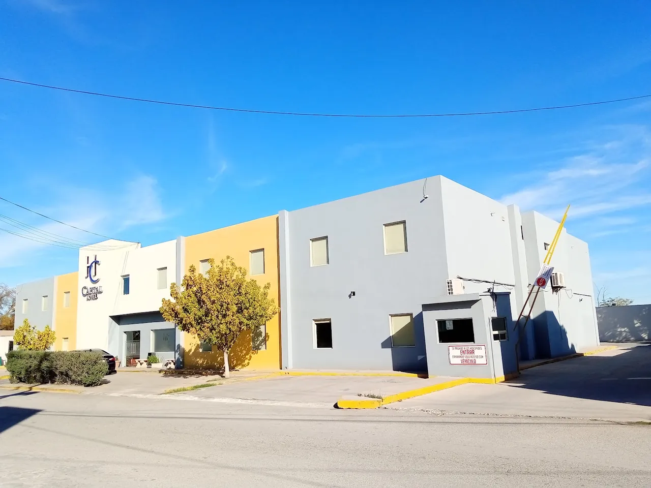 Fachada de Capital Hotel Monclova, blanca, amarilla y gris, bajo un cielo azul despejado