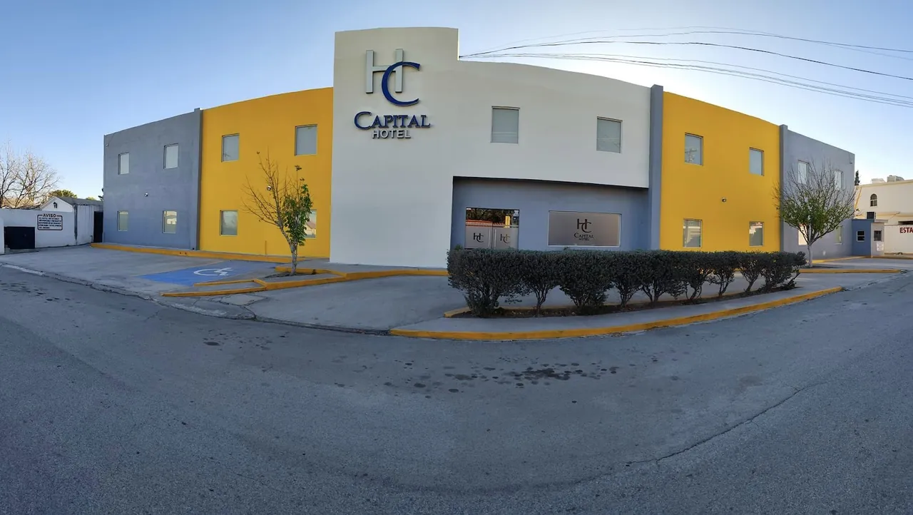 Fachada panorámica de Capital Hotel Monclova, blanca, amarilla y gris, con el logo en lo alto