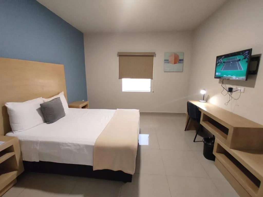 Habitación con cama, cabecera de madera, muro azul, escritorio y smart TV en la pared