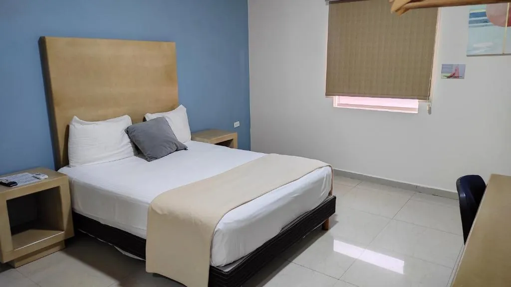 Habitación con cama tendida en blanco, cabecera de madera y muro azul