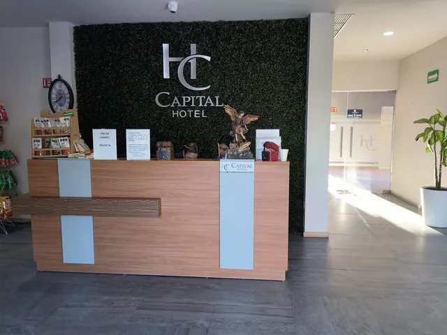 Mostrador de recepción frente al muro verde con el logo de Capital Hotel