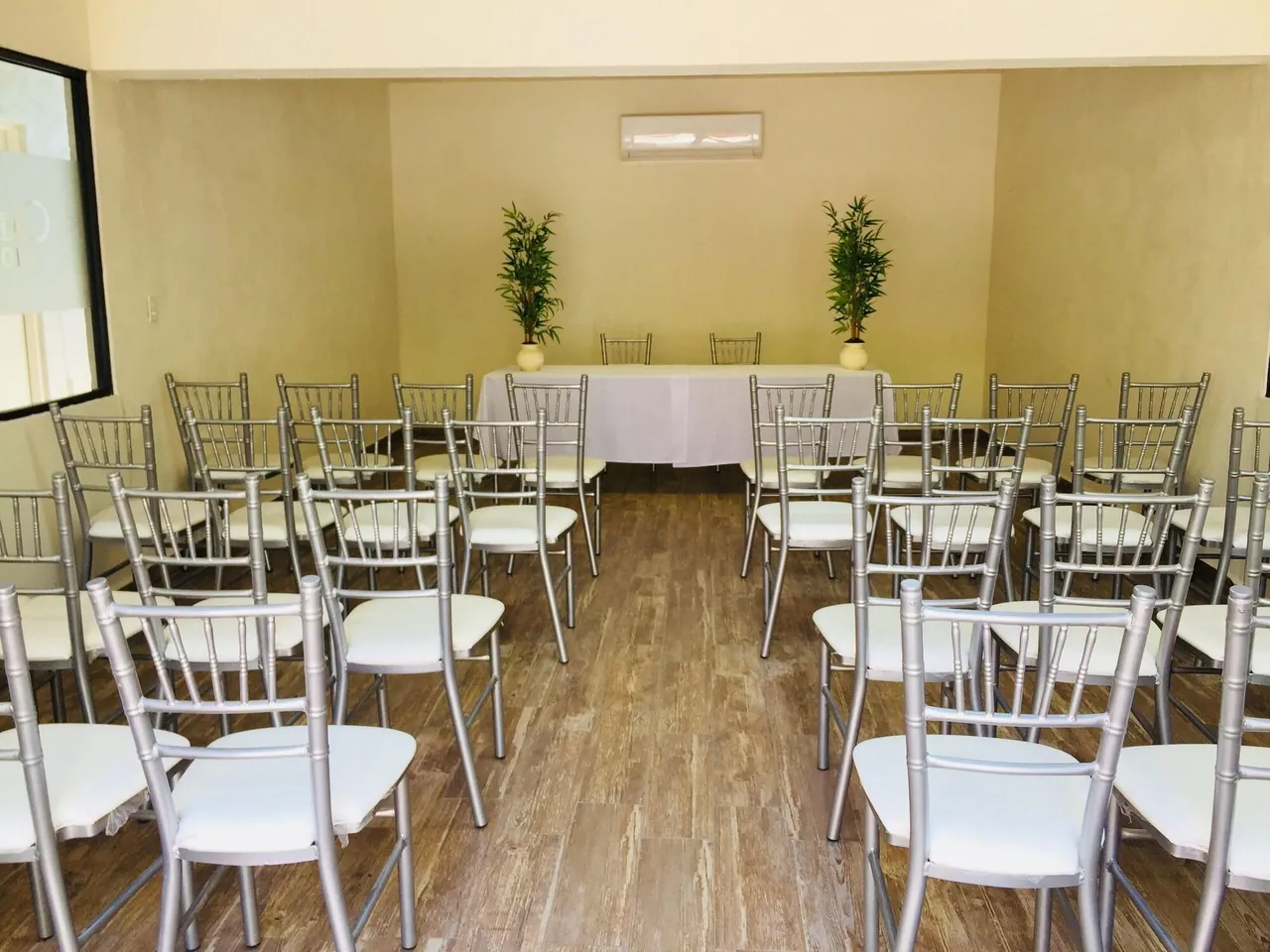 Sala de juntas con sillas plateadas en filas y mesa con mantel blanco