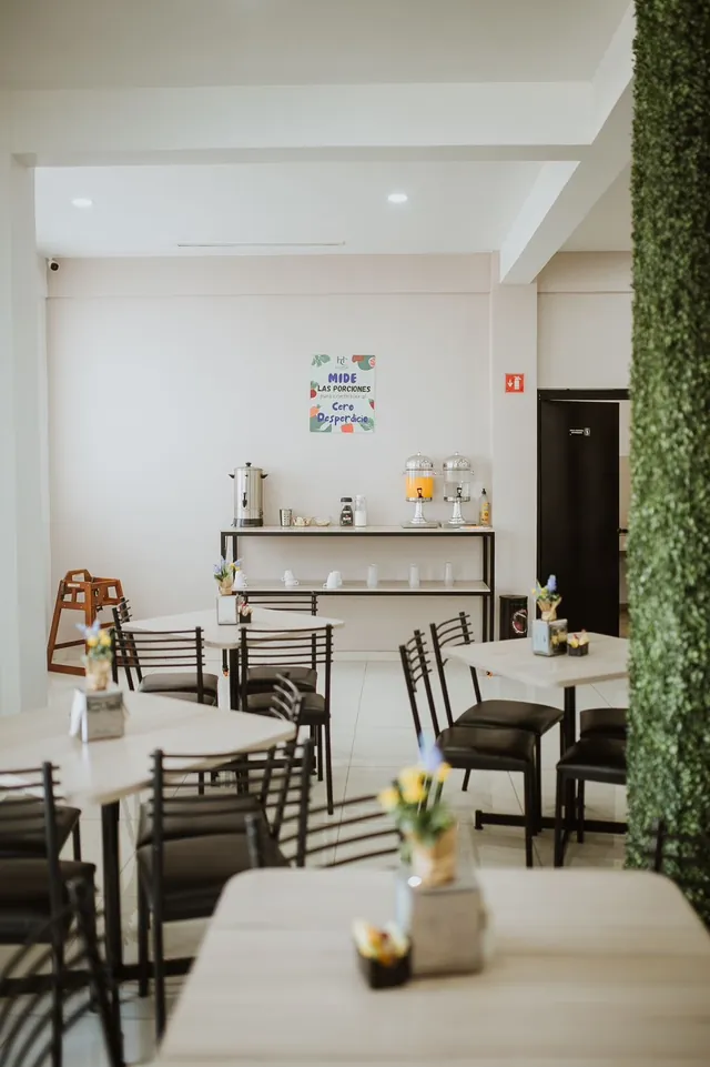 Desayunador con mesas claras, sillas negras y flores amarillas junto al muro verde