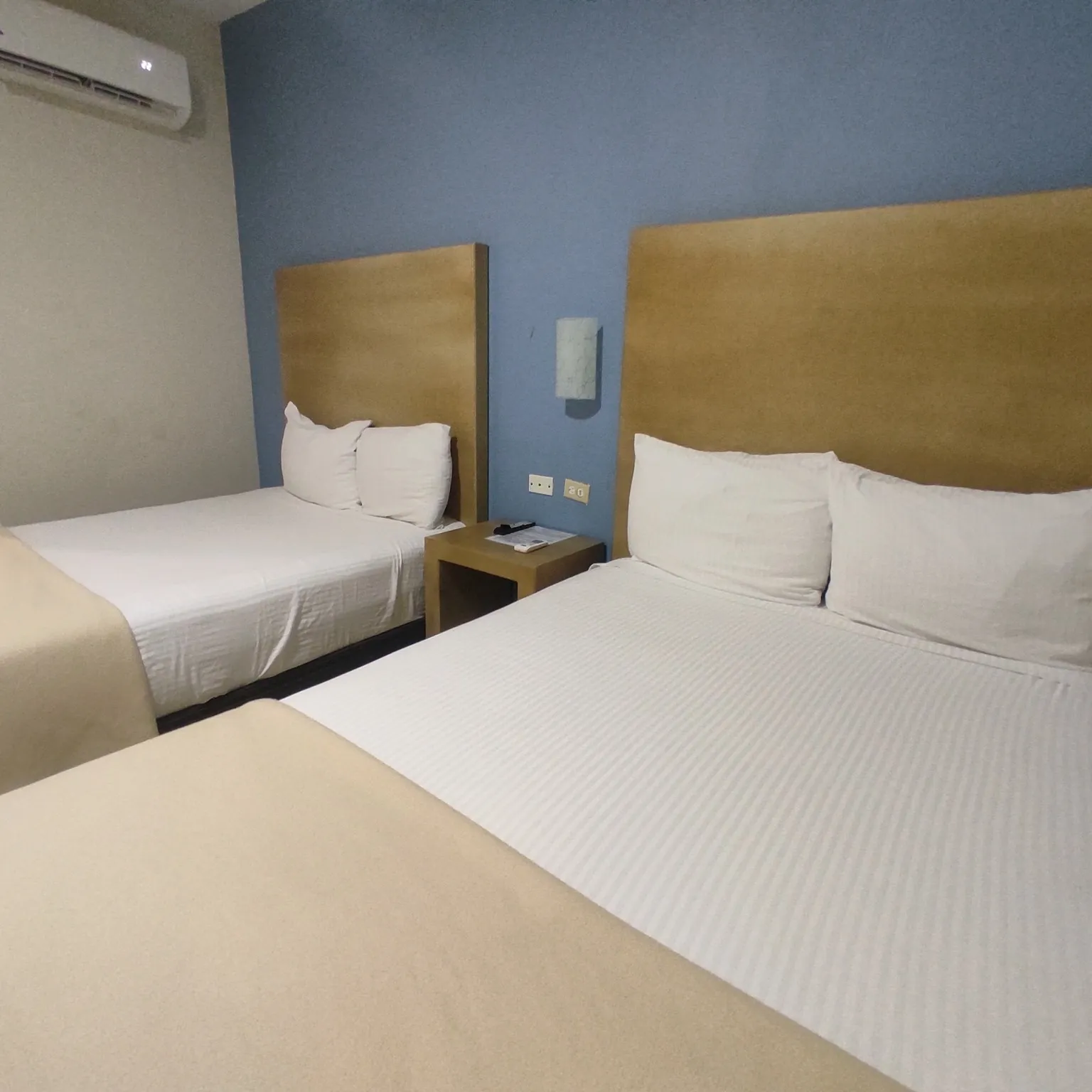 Habitación con dos camas tendidas en blanco, cabeceras de madera y muro azul