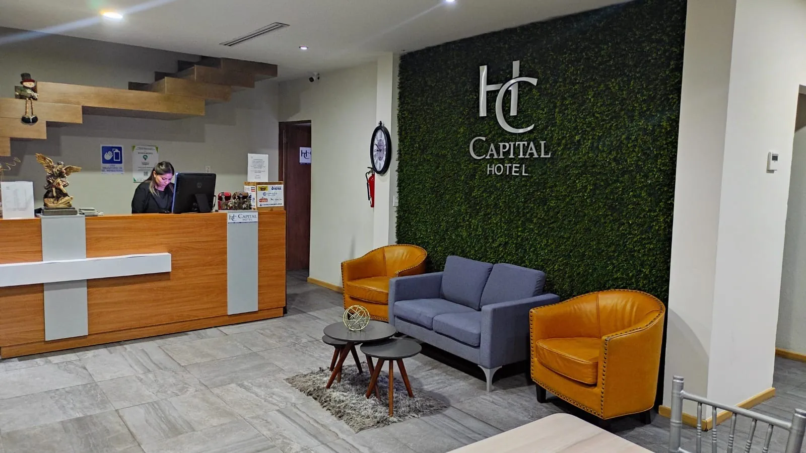 Recepción de Capital Hotel Monclova con muro verde, logo HC, sillones color miel y mostrador de madera