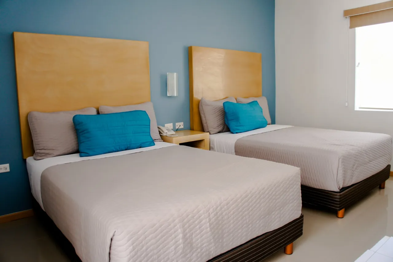 Habitación doble con dos camas, cojines turquesa, cabeceras de madera y muro azul