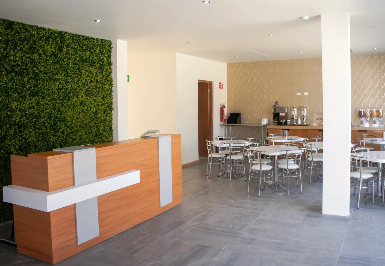 Desayunador amplio con mesas, sillas y barra de café junto al muro verde